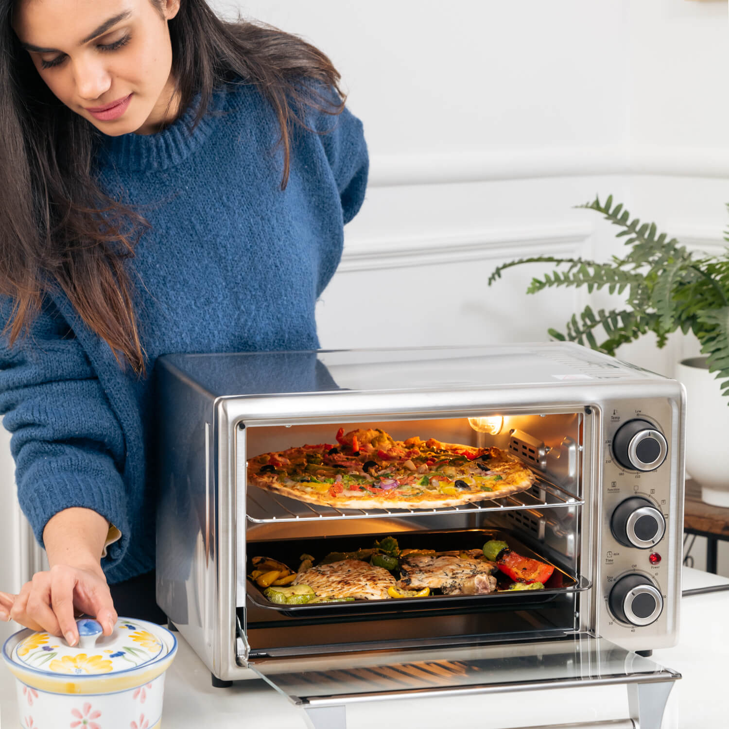 Osmon OTG Oven Showcasing Women standing while using OTG to grill the Pizza and veggies