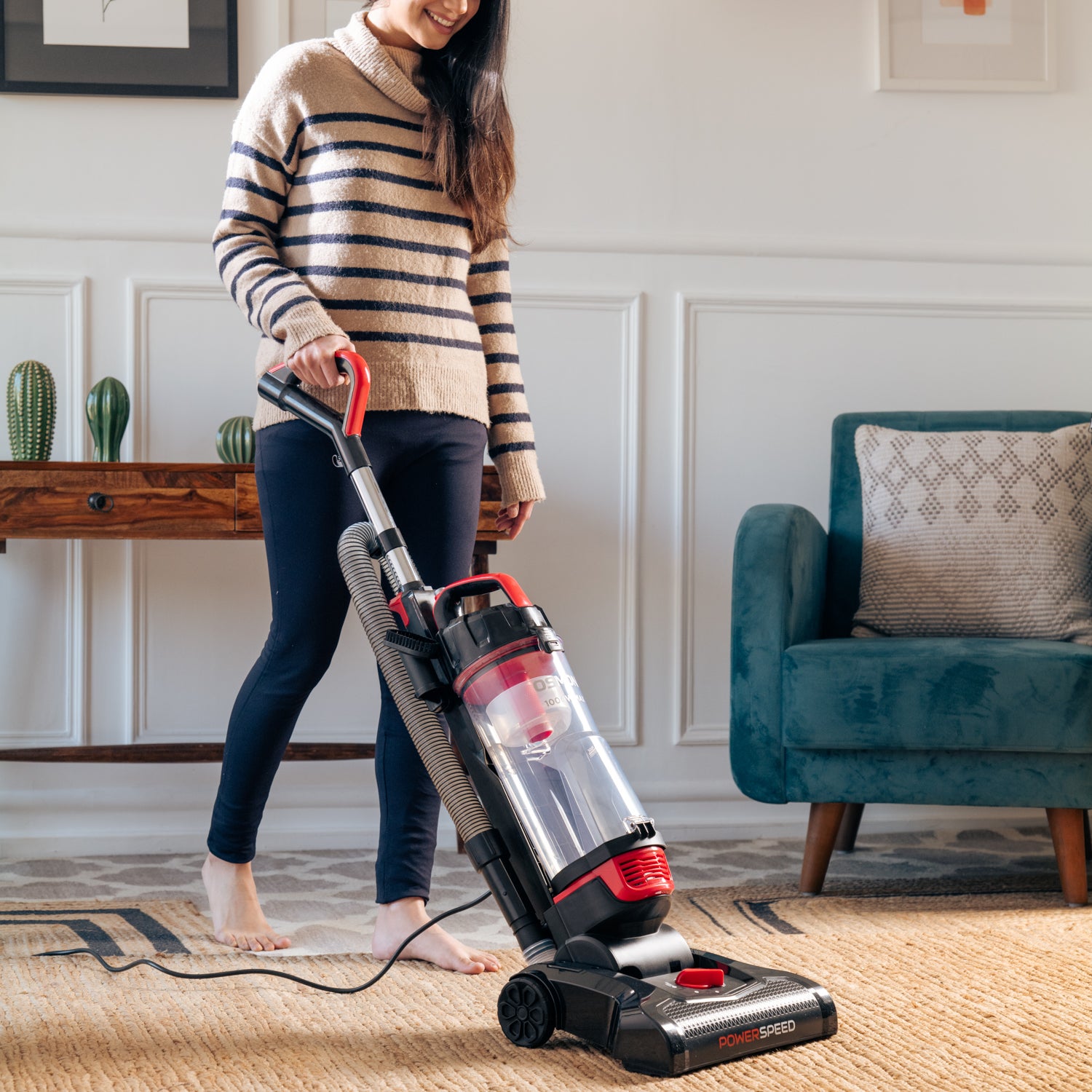 A sleek Red and black vacuum cleaner, the OS 26UBL, Showcasing women standing against a backdrop of a clean and tidy living room using our Powerspeed Upright Vacuum